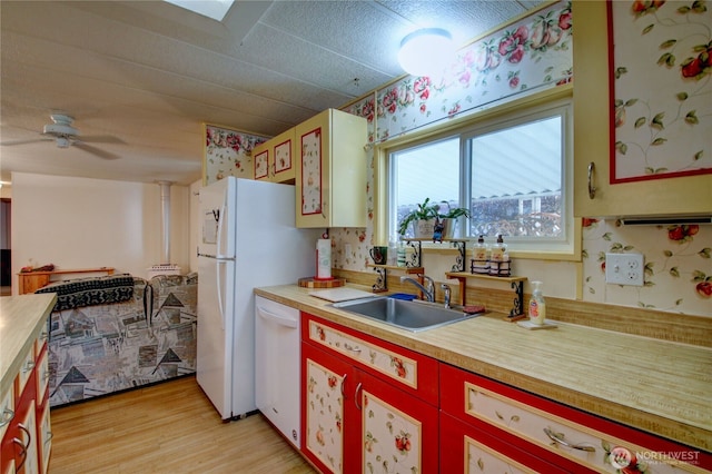 kitchen featuring light wood finished floors, wooden counters, a ceiling fan, white dishwasher, and a sink