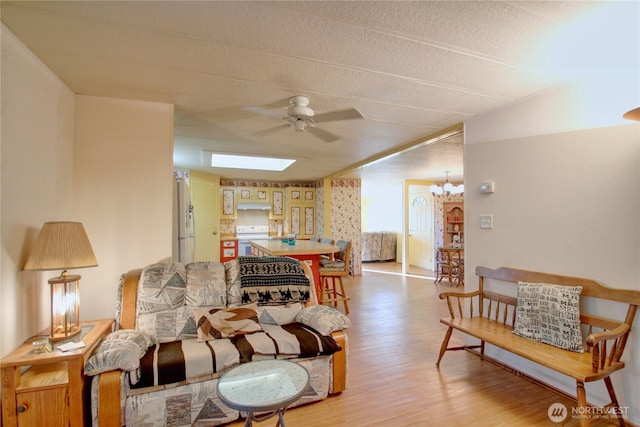 living room with a skylight, light wood finished floors, and ceiling fan with notable chandelier