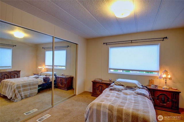 carpeted bedroom with a textured ceiling, visible vents, and a closet