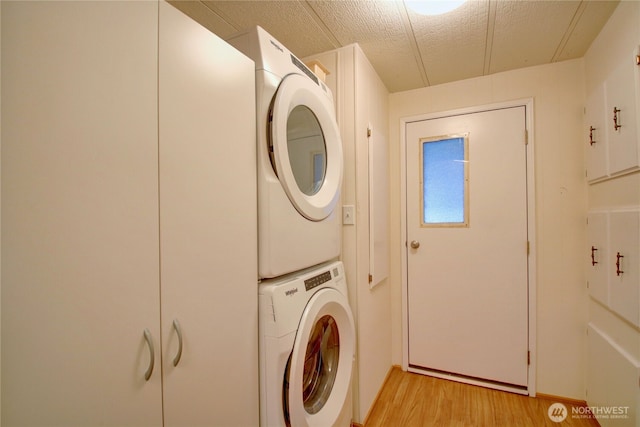 laundry area with light wood-style floors, stacked washer / drying machine, laundry area, and a textured ceiling