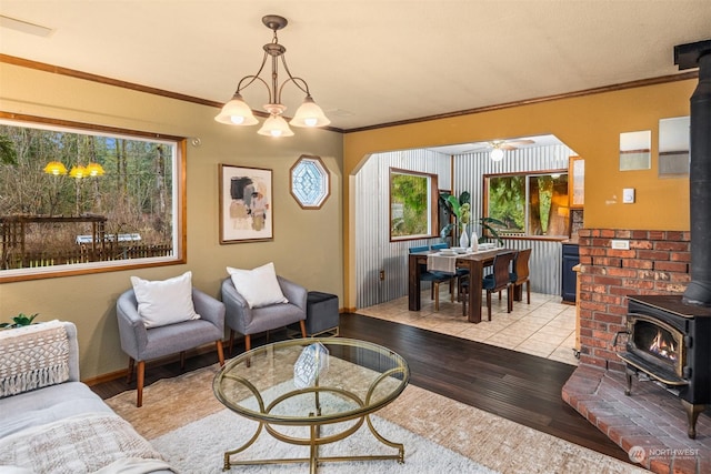 living room with ceiling fan with notable chandelier, light wood-type flooring, a wood stove, and ornamental molding