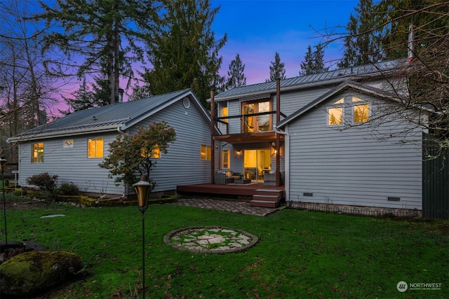 back house at dusk with a deck and a lawn