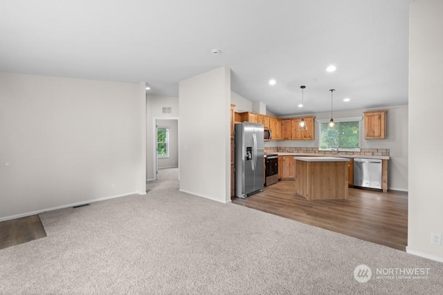 kitchen with decorative light fixtures, light colored carpet, appliances with stainless steel finishes, and a kitchen island