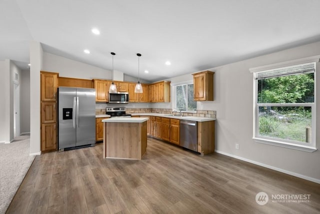 kitchen featuring decorative light fixtures, vaulted ceiling, hardwood / wood-style floors, a center island, and stainless steel appliances