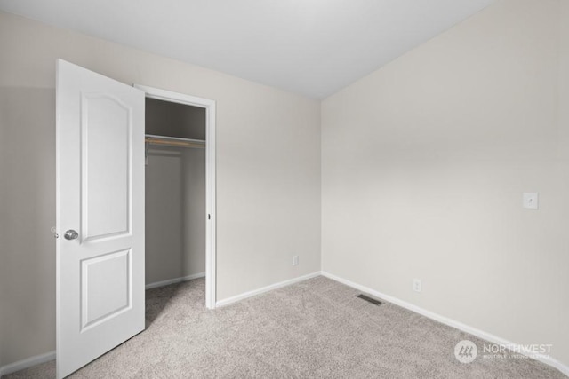 unfurnished bedroom with light colored carpet and a closet