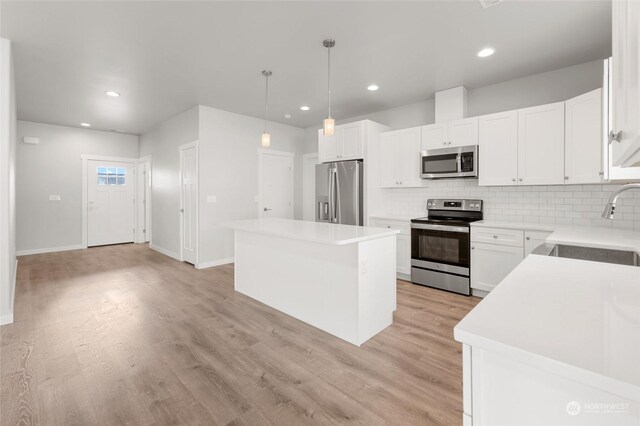 kitchen with stainless steel appliances, sink, white cabinetry, a kitchen island, and pendant lighting