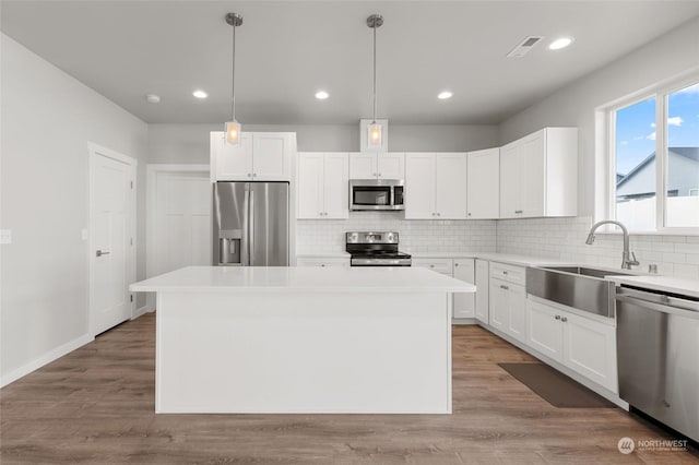 kitchen with appliances with stainless steel finishes, pendant lighting, white cabinetry, and a kitchen island