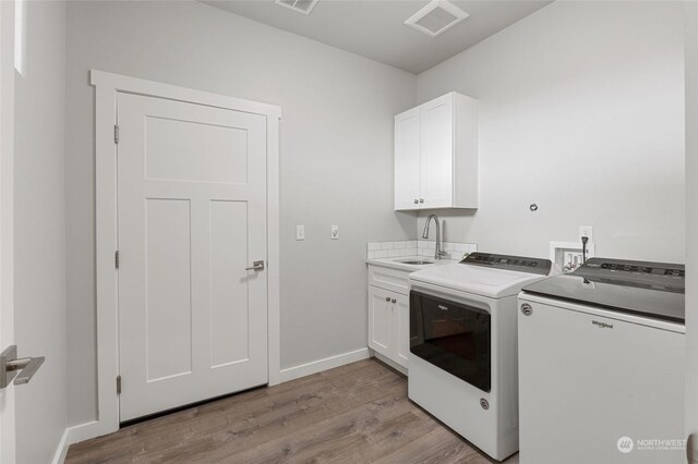 clothes washing area with washer and dryer, cabinets, light hardwood / wood-style flooring, and sink