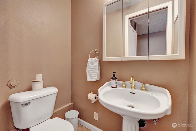 bathroom featuring toilet, a textured ceiling, and sink