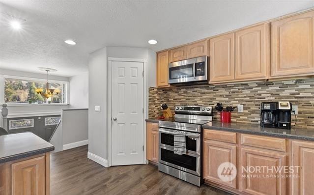 kitchen featuring dark wood-type flooring, backsplash, hanging light fixtures, and appliances with stainless steel finishes