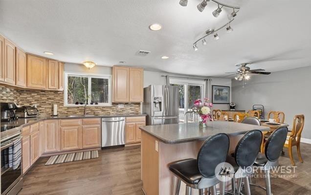 kitchen with ceiling fan, backsplash, a kitchen island, appliances with stainless steel finishes, and light brown cabinets