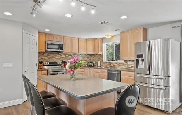 kitchen with a kitchen bar, stainless steel appliances, light brown cabinets, a kitchen island, and light hardwood / wood-style flooring