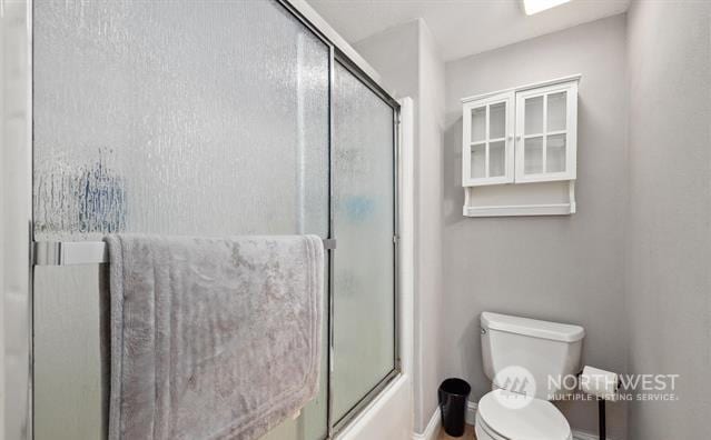 bathroom with toilet and bath / shower combo with glass door