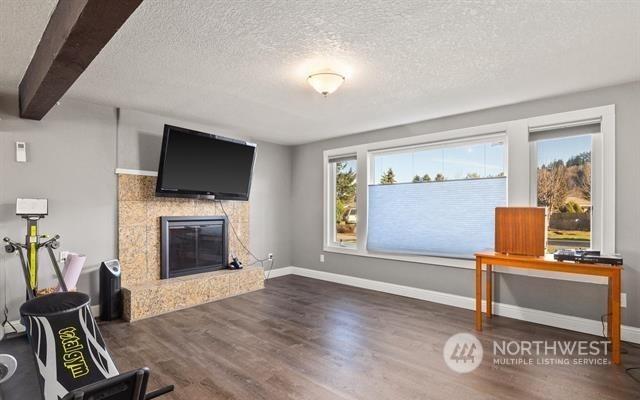 interior space featuring a textured ceiling, dark wood-type flooring, beam ceiling, and a fireplace