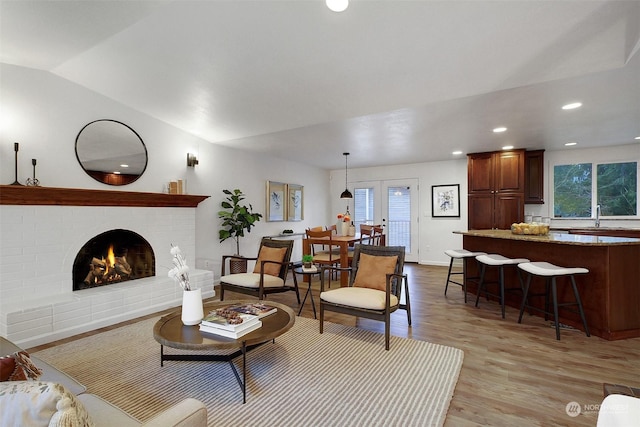 living room with a brick fireplace, light wood-type flooring, french doors, and a wealth of natural light