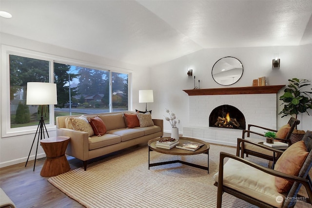 living room featuring wood-type flooring, a brick fireplace, and vaulted ceiling