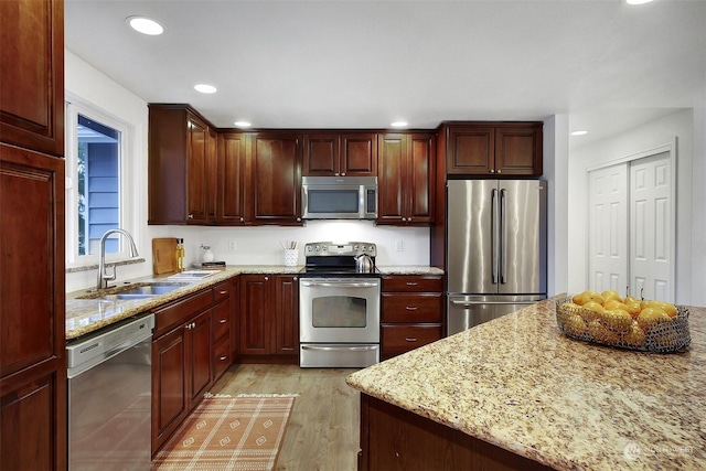 kitchen featuring sink, stainless steel appliances, light hardwood / wood-style flooring, and light stone counters