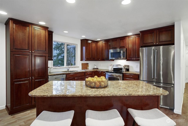 kitchen with light stone countertops, a center island, stainless steel appliances, a breakfast bar, and sink