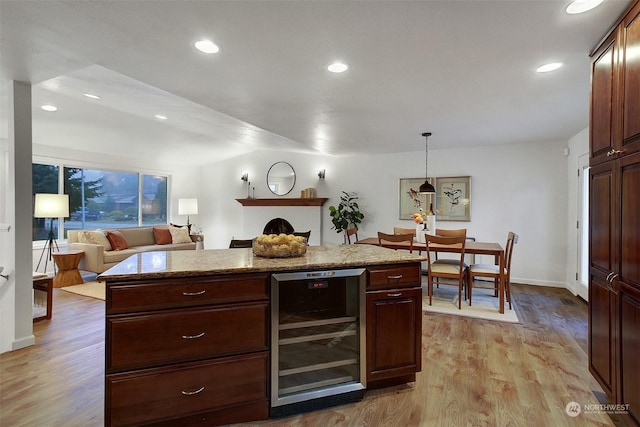 kitchen featuring light stone countertops, hanging light fixtures, beverage cooler, light wood-type flooring, and a fireplace