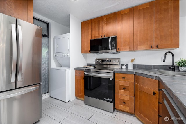 kitchen with sink, a textured ceiling, stacked washer and clothes dryer, and stainless steel appliances