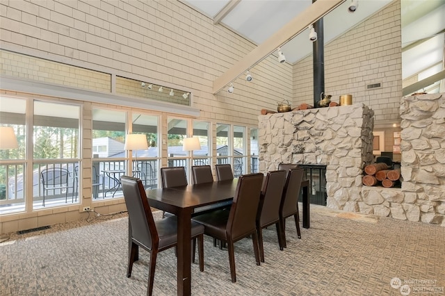 carpeted dining space with high vaulted ceiling, a wealth of natural light, beam ceiling, and a stone fireplace