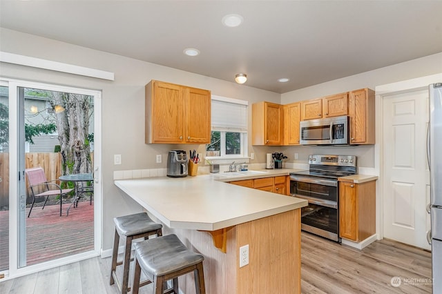 kitchen with a breakfast bar area, stainless steel appliances, light wood-type flooring, kitchen peninsula, and sink