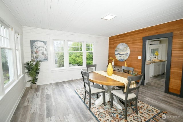 dining area featuring light hardwood / wood-style floors, a wall mounted air conditioner, wood walls, and sink