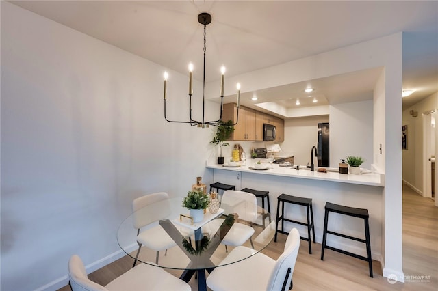 dining area with a raised ceiling, sink, an inviting chandelier, and light hardwood / wood-style flooring