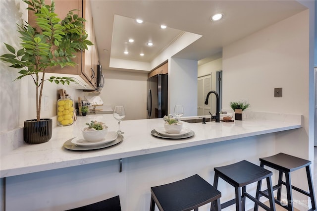 kitchen with black refrigerator, sink, kitchen peninsula, a breakfast bar, and a tray ceiling