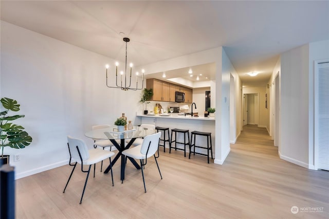 dining space featuring sink, light hardwood / wood-style flooring, and a notable chandelier