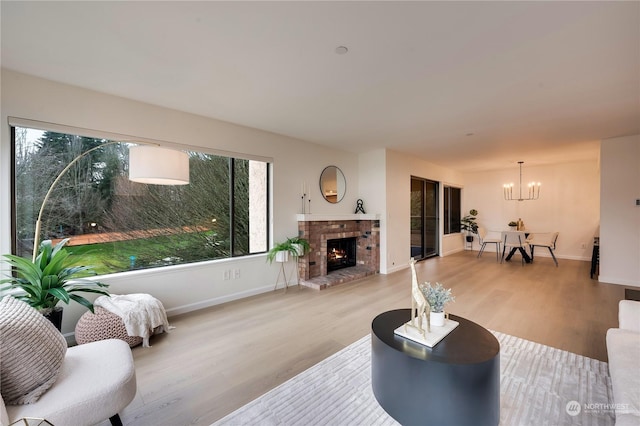 living room with light wood-type flooring, a brick fireplace, and a notable chandelier