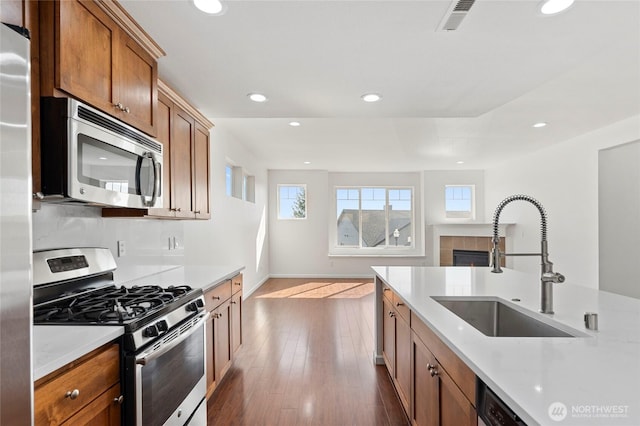 kitchen with brown cabinets, dark wood-type flooring, a sink, appliances with stainless steel finishes, and light countertops