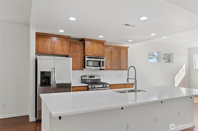 kitchen with visible vents, light countertops, appliances with stainless steel finishes, brown cabinetry, and a sink