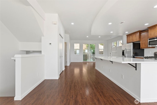 kitchen featuring a breakfast bar area, light countertops, brown cabinetry, stainless steel appliances, and a sink