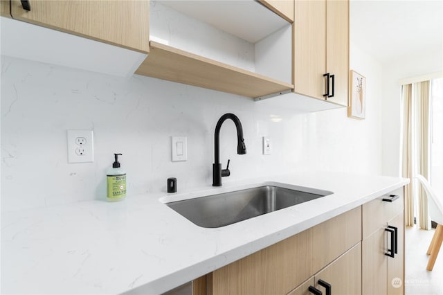 kitchen with sink, light brown cabinetry, light stone counters, and decorative backsplash