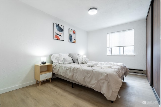 bedroom with a baseboard heating unit and light hardwood / wood-style flooring