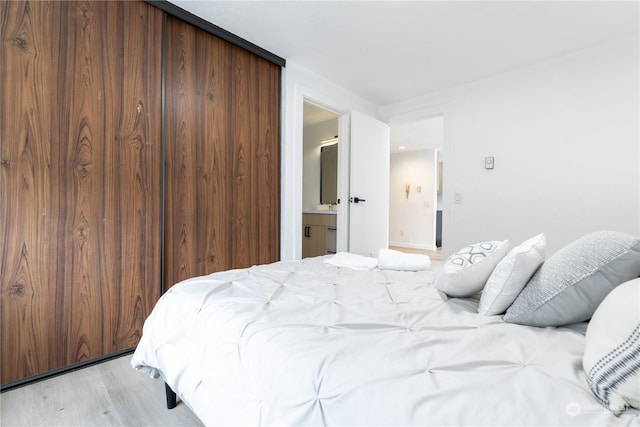 bedroom with ensuite bath, light wood-type flooring, and a closet