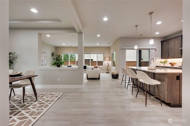 kitchen with a kitchen breakfast bar, light hardwood / wood-style floors, sink, dark brown cabinets, and decorative light fixtures