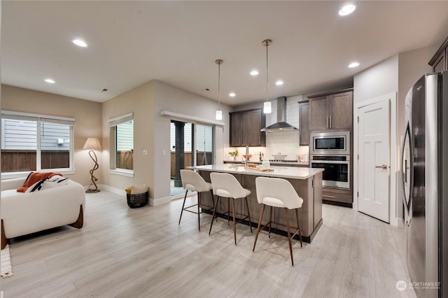 kitchen featuring stainless steel appliances, dark brown cabinetry, pendant lighting, and wall chimney exhaust hood