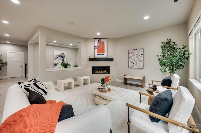 living room with a tiled fireplace and light wood-type flooring