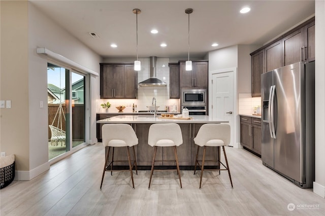 kitchen with stainless steel appliances, wall chimney range hood, pendant lighting, and dark brown cabinetry