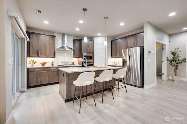 kitchen with decorative light fixtures, wall chimney exhaust hood, backsplash, dark brown cabinets, and appliances with stainless steel finishes