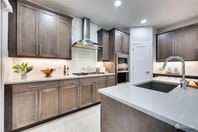 kitchen featuring appliances with stainless steel finishes, dark brown cabinets, sink, and wall chimney exhaust hood