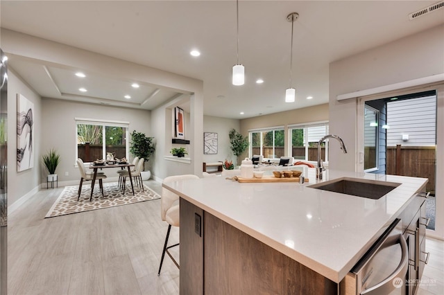 kitchen with dishwasher, a kitchen island with sink, light hardwood / wood-style floors, pendant lighting, and sink