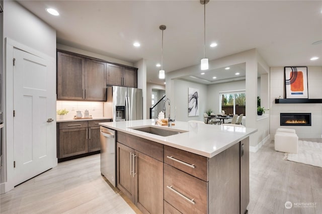 kitchen with sink, decorative light fixtures, a fireplace, a kitchen island with sink, and appliances with stainless steel finishes