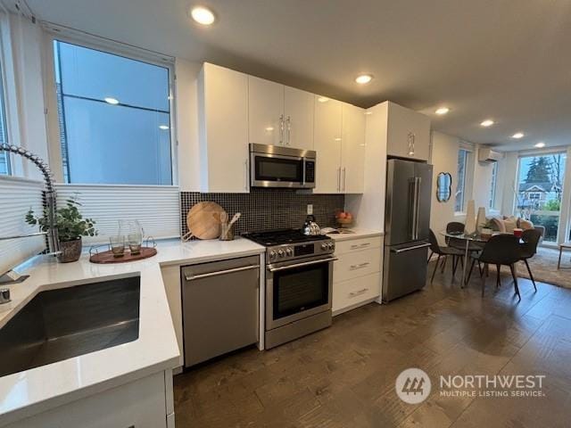 kitchen featuring dark wood-type flooring, stainless steel appliances, decorative backsplash, white cabinetry, and sink