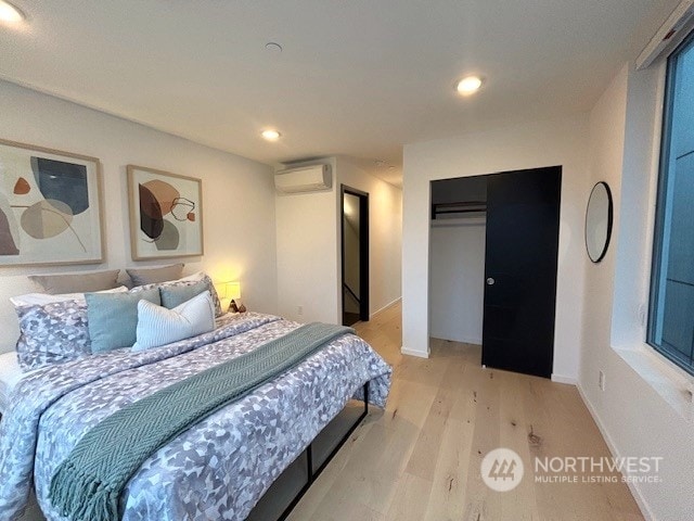 bedroom with an AC wall unit, a closet, and light hardwood / wood-style floors