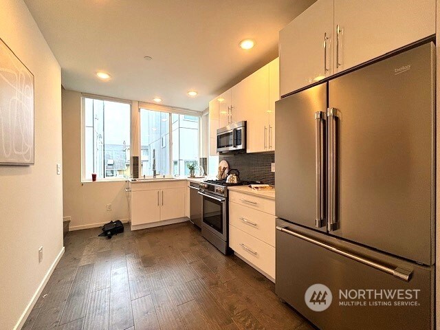 kitchen featuring tasteful backsplash, high quality appliances, dark wood-type flooring, white cabinets, and sink