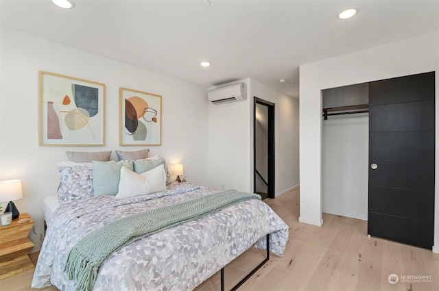 bedroom with a closet, an AC wall unit, and light hardwood / wood-style flooring