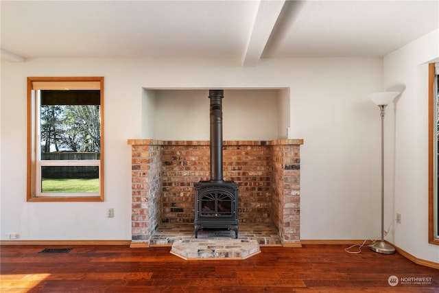 unfurnished living room with beamed ceiling, hardwood / wood-style flooring, and a wood stove